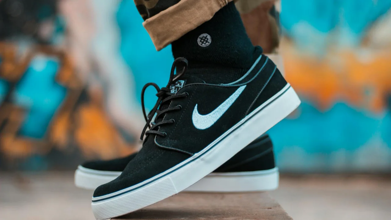 A close-up of a person wearing black Nike trainers with white soles, standing on a ledge.